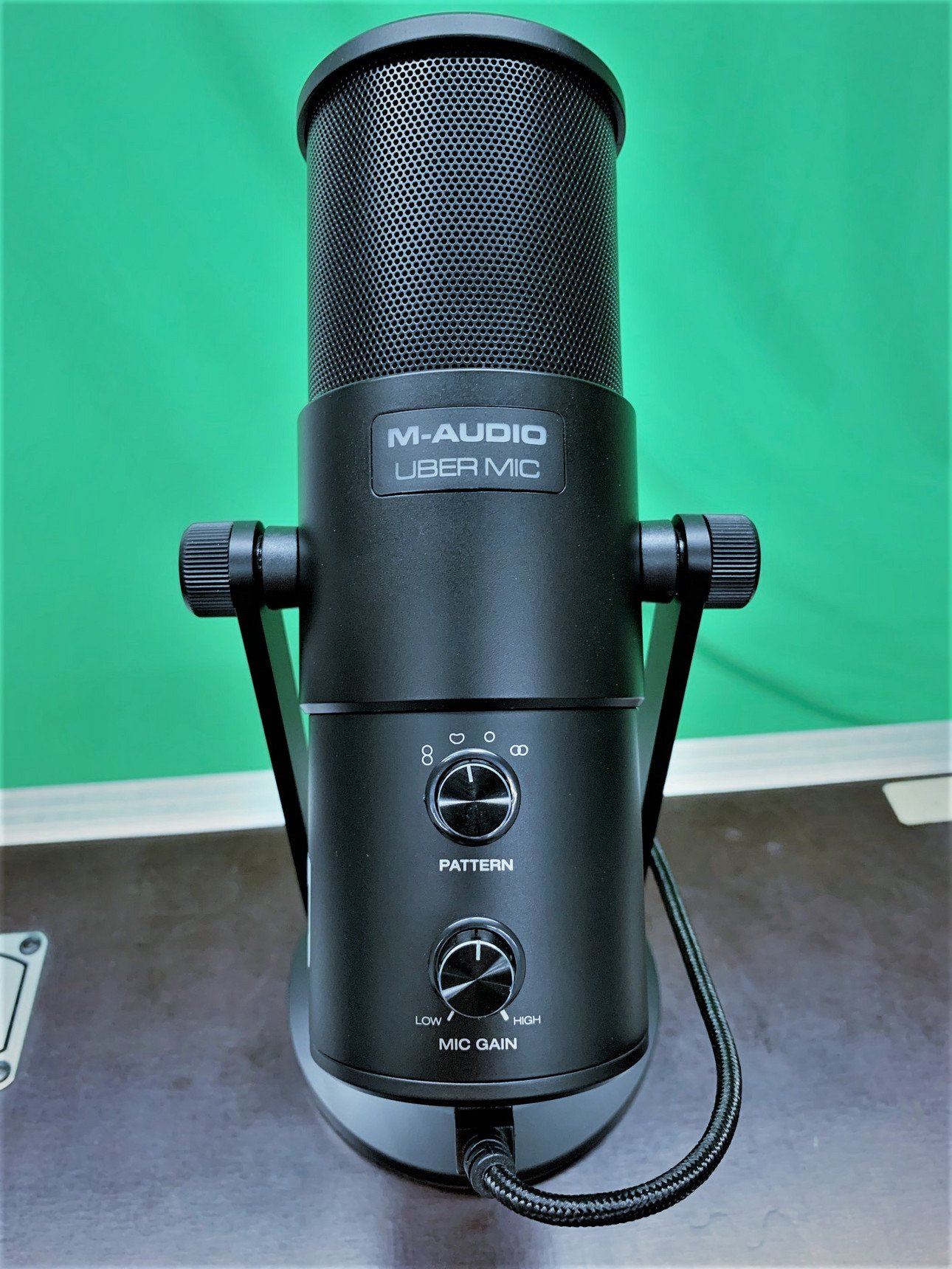 Hochwertiges Studio-Mikrofon f&uuml;r Podcasts und Aufnahmen mit verstellbaren Einstellungen f&uuml;r Pattern und Mic Gain auf einem Tisch vor gr&uuml;nem Hintergrund.