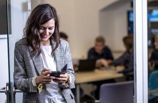 Eine Frau schaut auf ihr Handy, im Hintergrund diskutiert eine Gruppe von Menschen