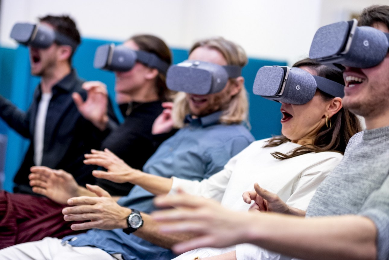 Mehrere Personen tragen Virtual-Reality-Brillen und zeigen begeisterte Reaktionen w&auml;hrend eines virtuellen Erlebnisses.