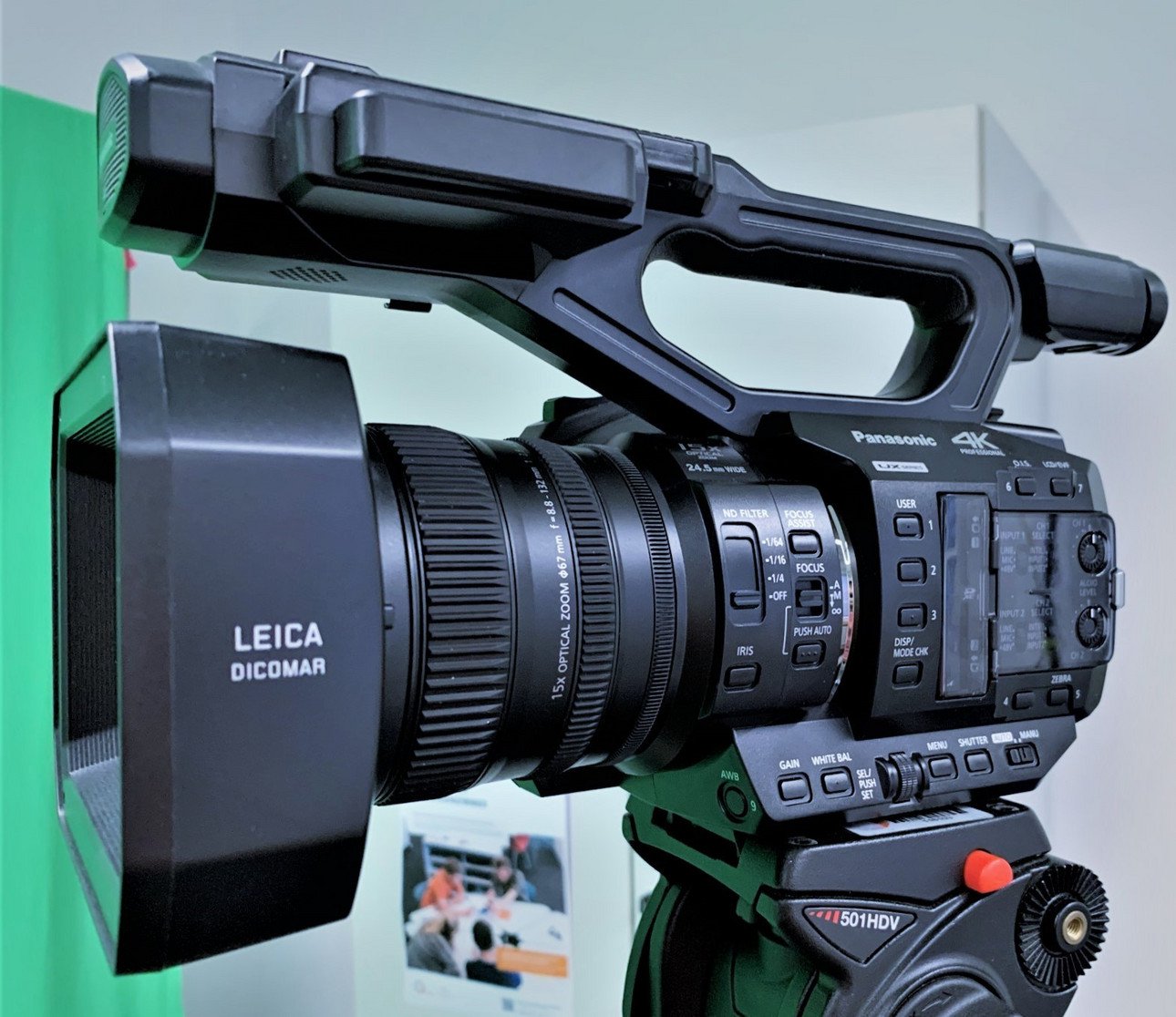 Detailaufnahme einer professionellen Videokamera mit sichtbaren Bedienelementen wie Zoomring, Fokusknopf und Men&uuml;buttons. Die Kamera ist mit einem robusten Stativ montiert und zeigt ein modernes Design f&uuml;r hochwertige Videoaufnahmen.