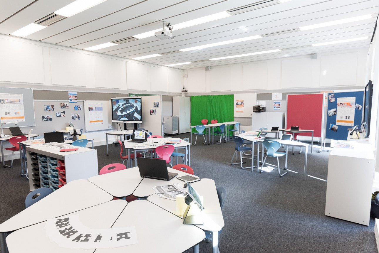 Ein modernes Klassenzimmer mit flexiblen Tischen, bunten St&uuml;hlen, Laptops und interaktiven Whiteboards. Die Ausstattung unterst&uuml;tzt digitales Lernen und kollaborative Arbeitsmethoden.