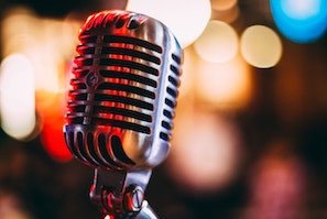 Klassisches Mikrofon f&uuml;r hochwertige Audioaufzeichnungen in Videoproduktionen, scharf im Vordergrund mit unscharfem, farbigem Hintergrund. Perfekt f&uuml;r optimierte Tonqualit&auml;t in visuellen Medien.